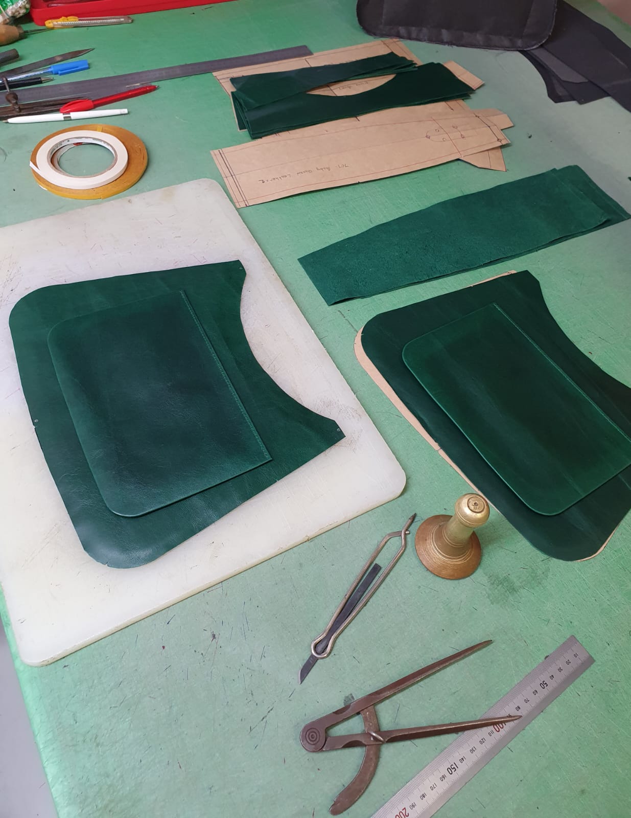 Green leather pieces being cut with patterns and tools in workshop